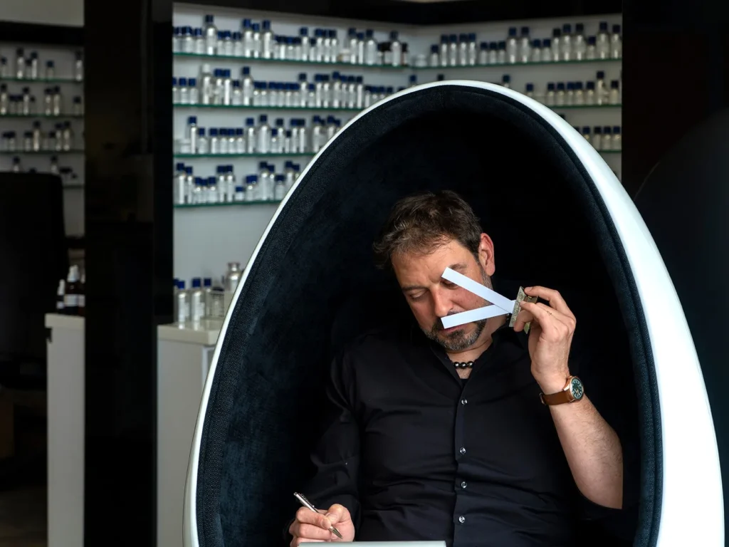 andreas wilhelm sniffing a perfume blotter while seated in a pod chair